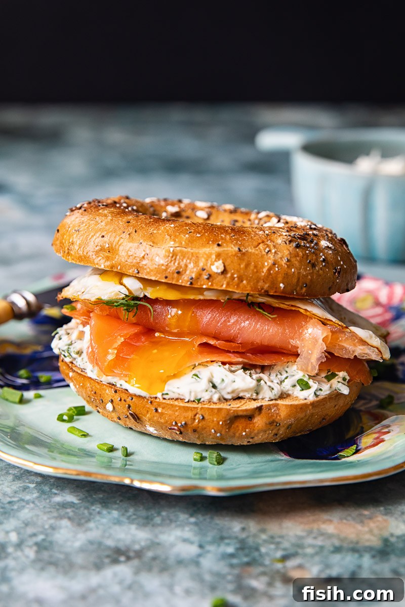 A vibrant, fully assembled breakfast bagel sandwich with smoked salmon, herbed cream cheese, and a fried egg, ready to be enjoyed.