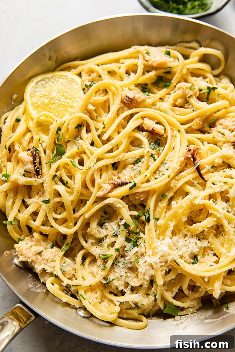 Close-up of freshly cooked linguine with crab in a stainless steel pan, garnished with herbs.
