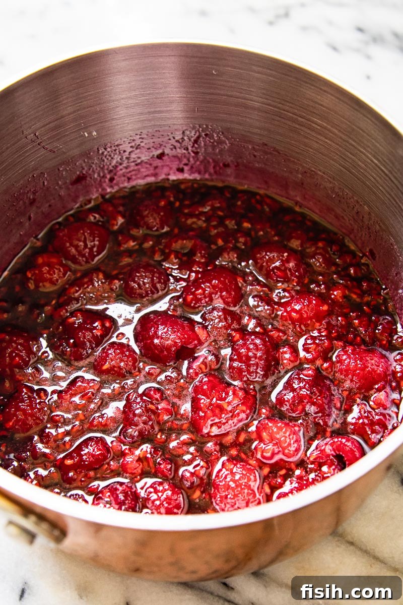 Raspberry compote simmering in a saucepan on the stovetop, showing the fruit pieces and syrupy consistency.