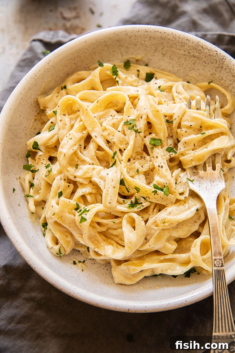 A bowl of freshly prepared fettuccine alfredo, generously sprinkled with vibrant fresh parsley, showcasing its creamy texture and inviting aroma.