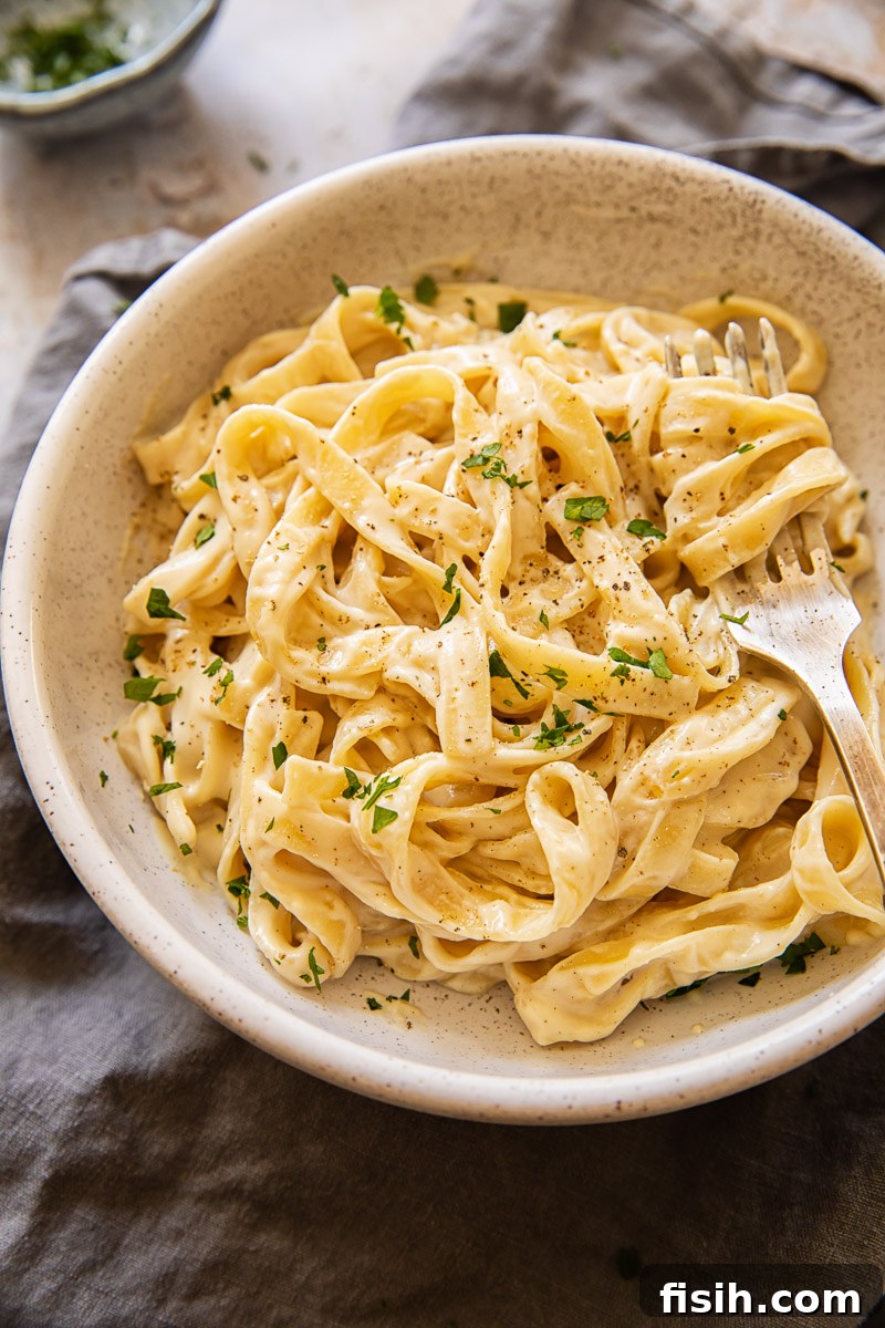 A vibrant top-down view of a classic plate of Fettuccine Alfredo, perfectly coated in a rich, creamy sauce.