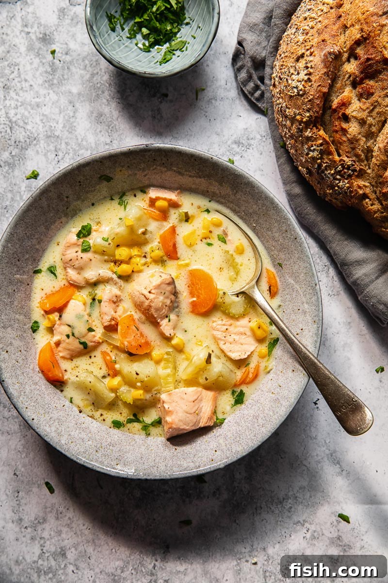 Hearty Salmon Chowder 3 A close-up of creamy salmon chowder in a rustic grey bowl with a spoon, accompanied by a loaf of crusty bread.