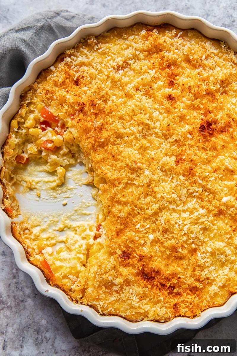 Top-down view of a golden scalloped corn casserole in a white baking dish, ready to be served, highlighting its crispy topping and creamy interior.
