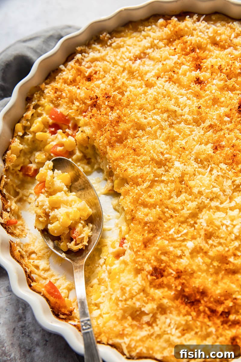 Creamy corn bake served in a white round baking dish with a spoon, showcasing its rich texture and inviting warmth.