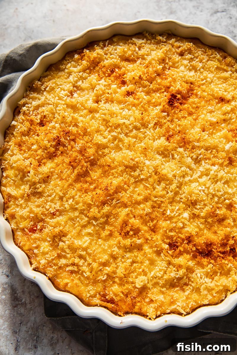 Close-up, top-down view of the golden, crispy topping on a scalloped corn gratin, showing the bubbly sauce underneath.