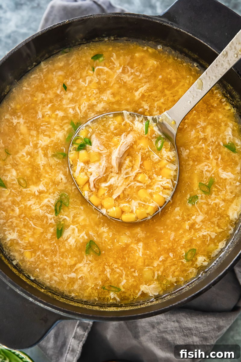 A large, rustic soup pot on the stovetop filled with simmering egg drop soup and tender shredded chicken pieces, hinting at the delicious meal to come.