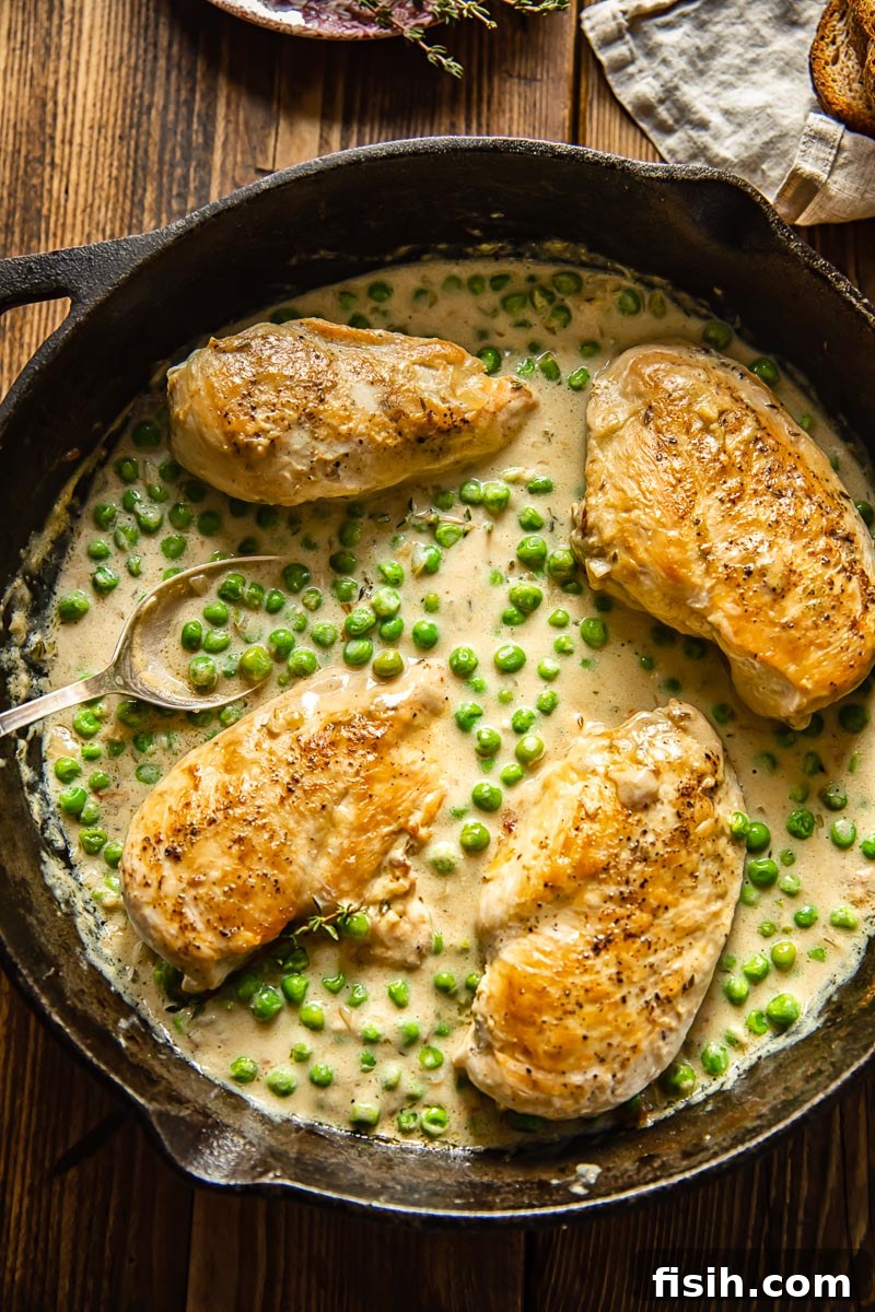 Velvety Chicken and Green Peas 2 Top down view of a cast iron pan featuring golden-brown chicken breasts and vibrant green peas bathed in a rich, creamy sauce.