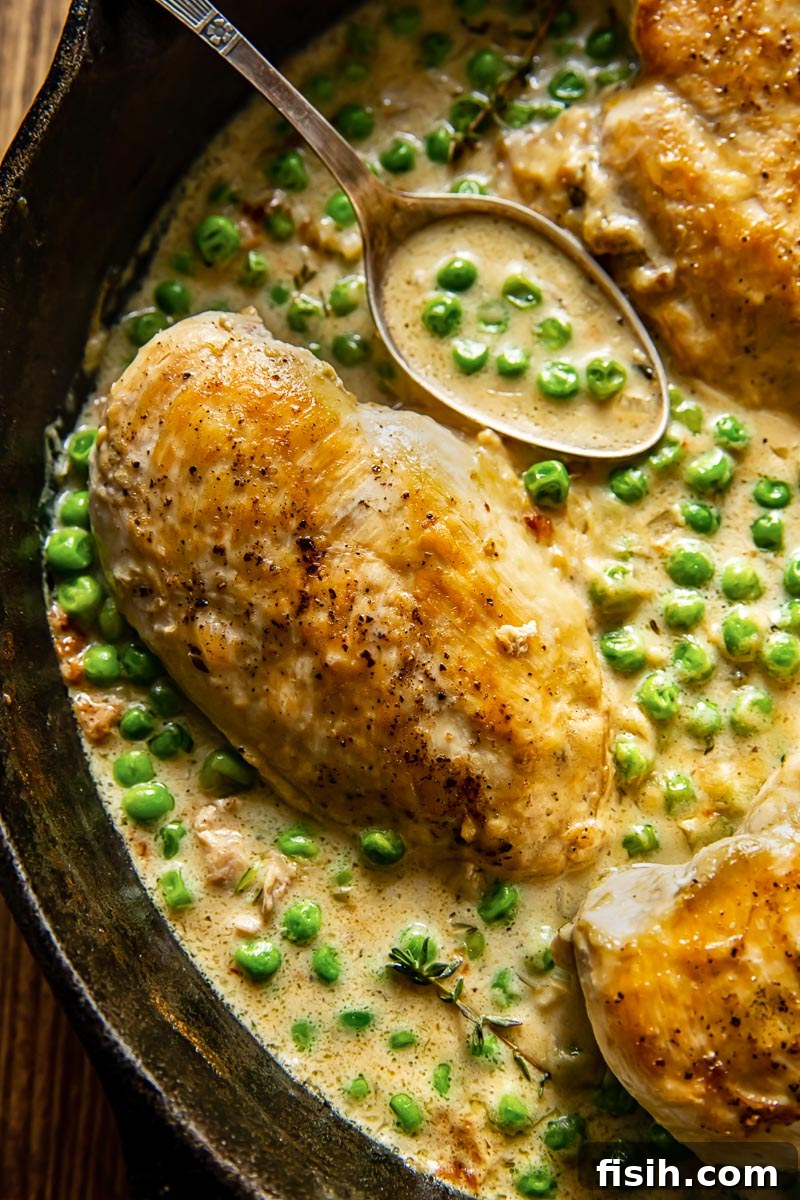 Velvety Chicken and Green Peas 3 Close-up view of a perfectly cooked chicken breast nestled in a creamy sauce with bright green peas, inviting a taste.