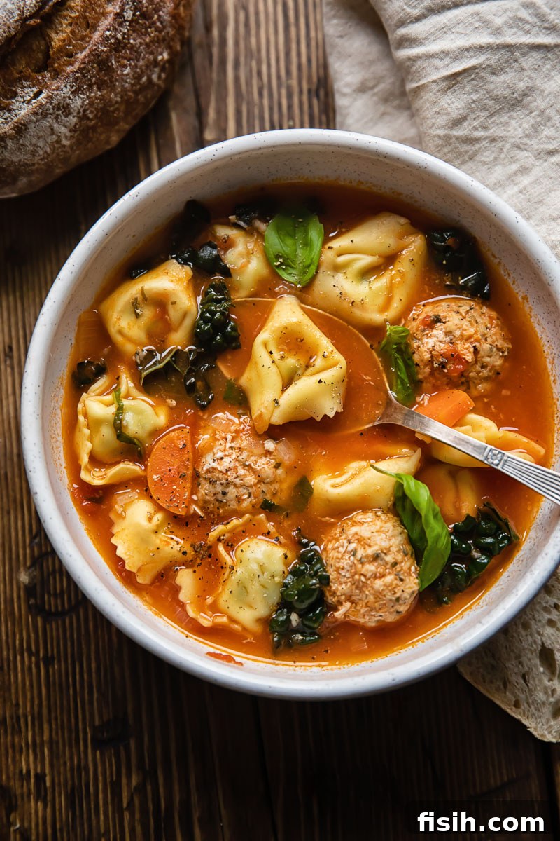 A steaming bowl of chicken meatball and tortellini soup, garnished with fresh herbs and a sprinkle of Parmesan cheese, highlighting its cozy and inviting nature.