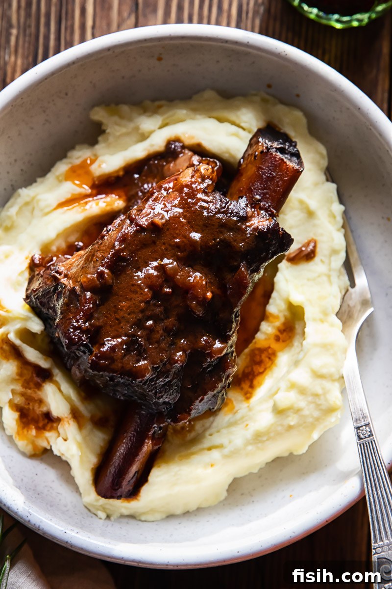 Tender beef short rib in a rich red wine sauce, served elegantly atop creamy mashed potatoes in a bowl, ready to be enjoyed.