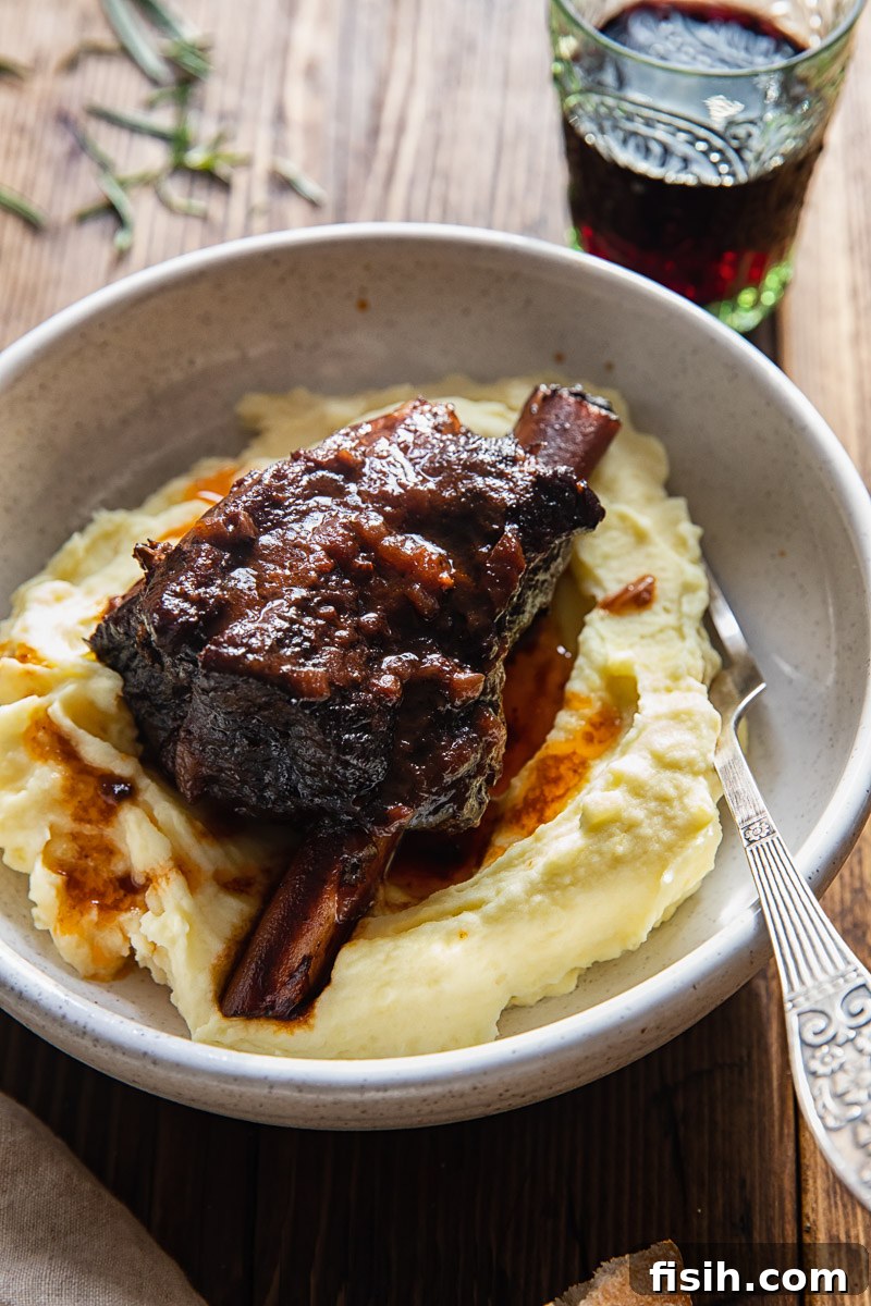 A beautifully plated braised short rib on a bed of mashed potatoes in a rustic bowl, accompanied by a glass of red wine, highlighting a perfect winter meal.