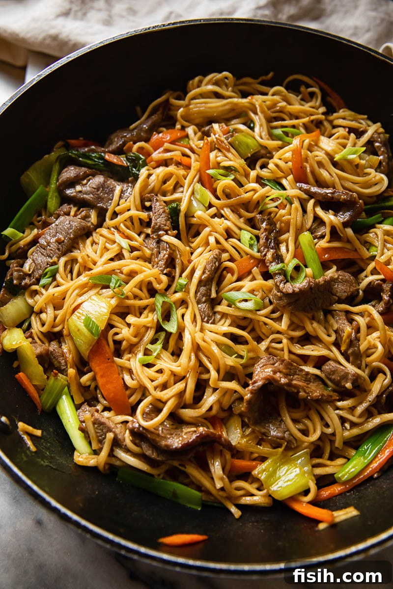 A vibrant top-down view of Beef Chow Mein, featuring tender steak slices, golden egg noodles, and colorful vegetables, served in a large wok, ready to be enjoyed.