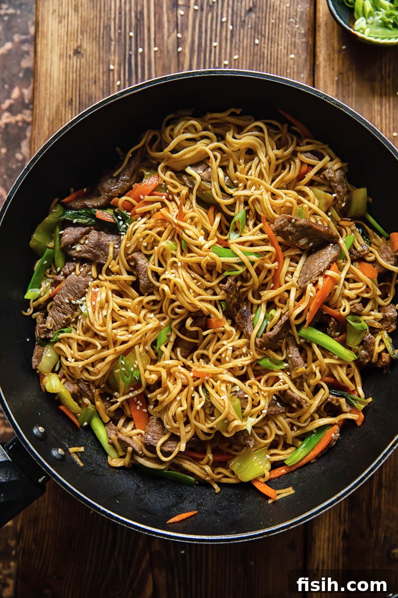 A close-up, top-down view of a generous serving of homemade Beef Chow Mein in a large wok, showcasing glossy egg noodles, thinly sliced beef, and colorful, crisp-tender vegetables like bok choy and carrots.