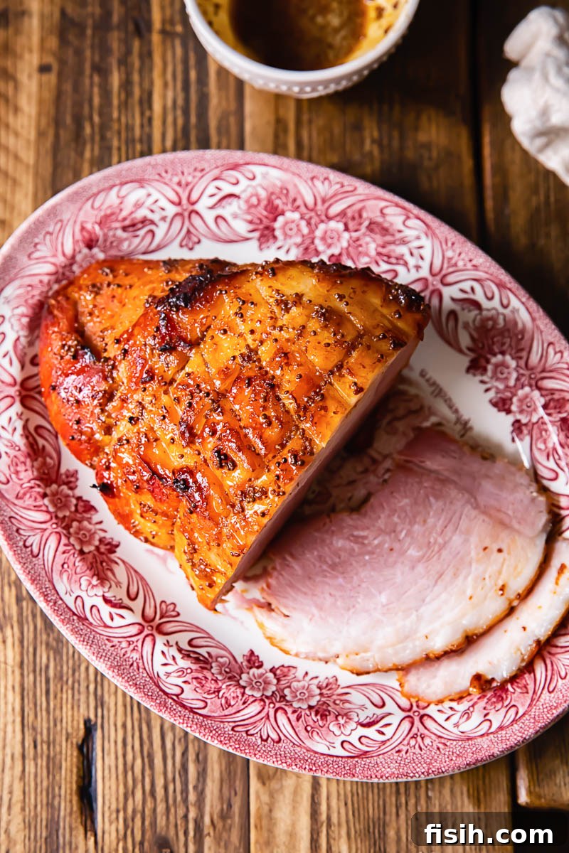 top down view of honey glazed ham on a platter, garnished with fresh herbs
