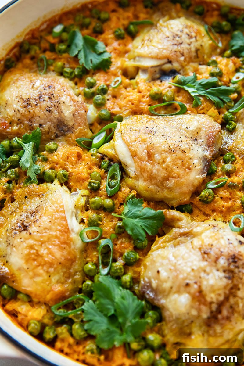 Golden-brown chicken thighs beautifully arranged on top of fragrant turmeric rice and green peas in a sturdy pan, ready to be baked.