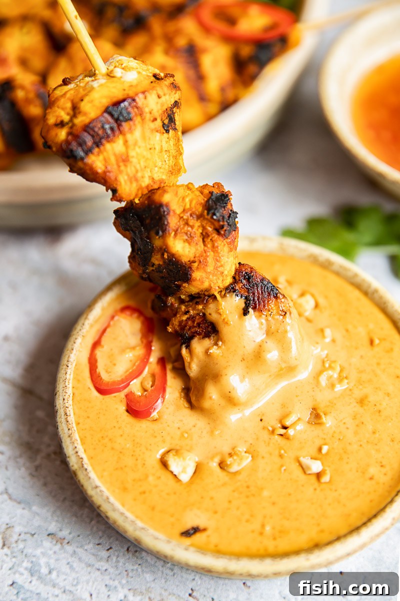 Simple Chicken Satay with Creamy Peanut Sauce 4 A close-up shot of a grilled chicken satay skewer being generously dipped into a small, creamy bowl of peanut sauce, emphasizing its perfect texture and color.