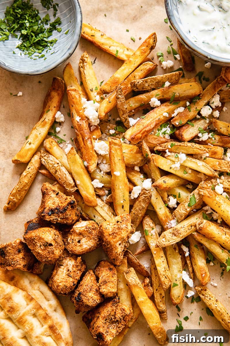 Zesty Air Fryer Greek Fries 3 Top-down view of a platter with Greek fries, grilled chicken souvlaki, warm pita bread, and a creamy yogurt dip