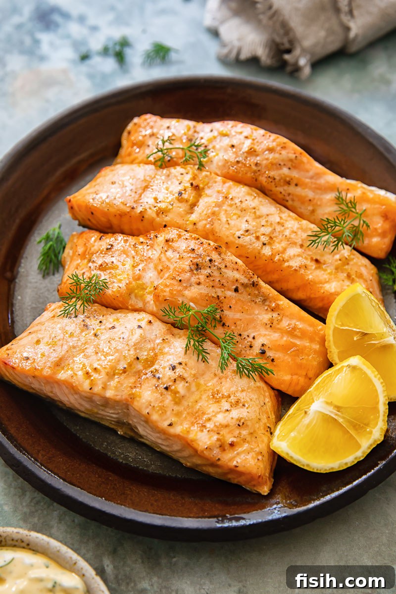 8-Minute Air Fryer Salmon with Zesty Lemon Dill Sauce 2 pieces of cooked salmon with lemon wedges on a plate