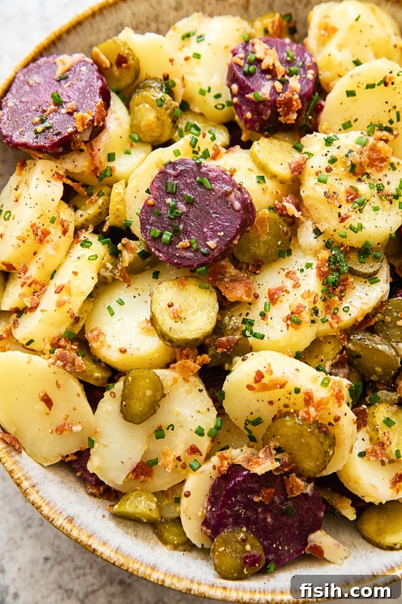 Close-up shot of German potato salad featuring crispy bacon bits, sliced pickles, and fresh chives, highlighting its texture and freshness