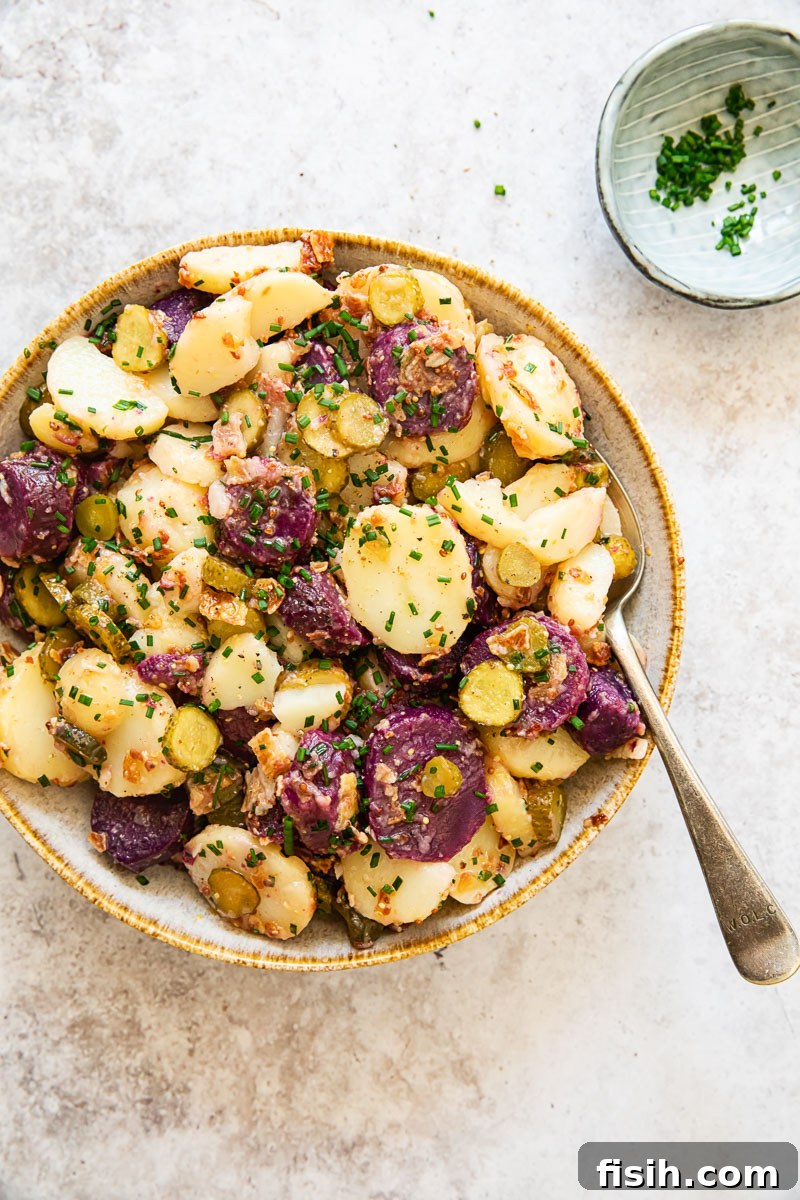 Generous bowl of German potato salad with white and purple potatoes, a serving spoon, and fresh chives, ready to be enjoyed
