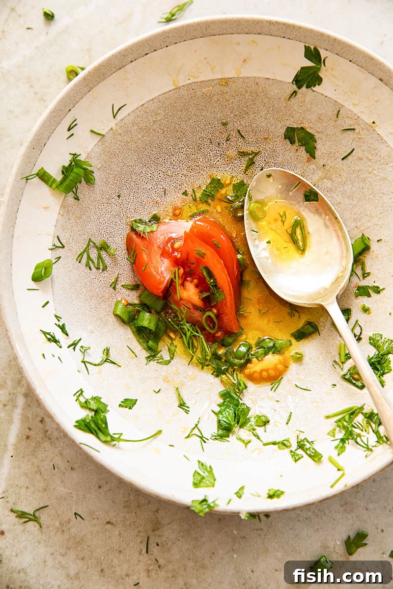 nearly empty salad bowl with salad dressing a tomato slice at the bottom, a spoon