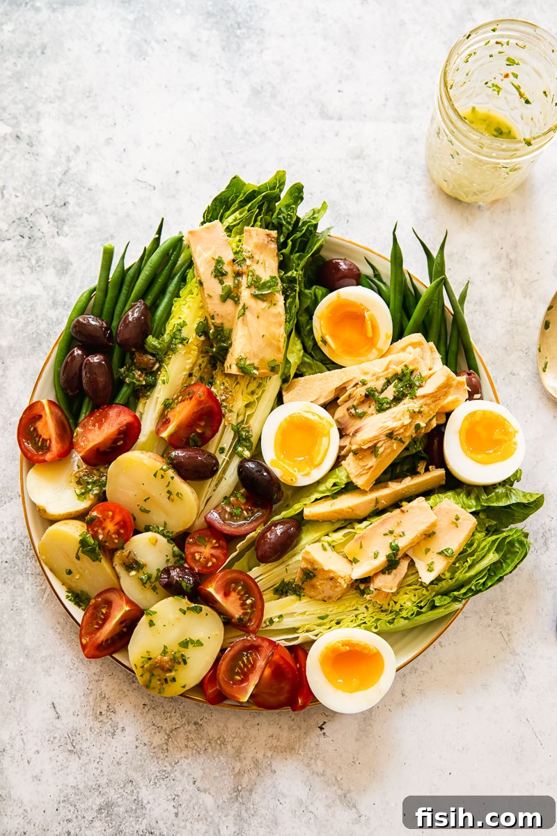 A vibrant top-down shot of a fully dressed Salade Nicoise, with a small bowl of vinaigrette placed beside it, ready to be enjoyed.