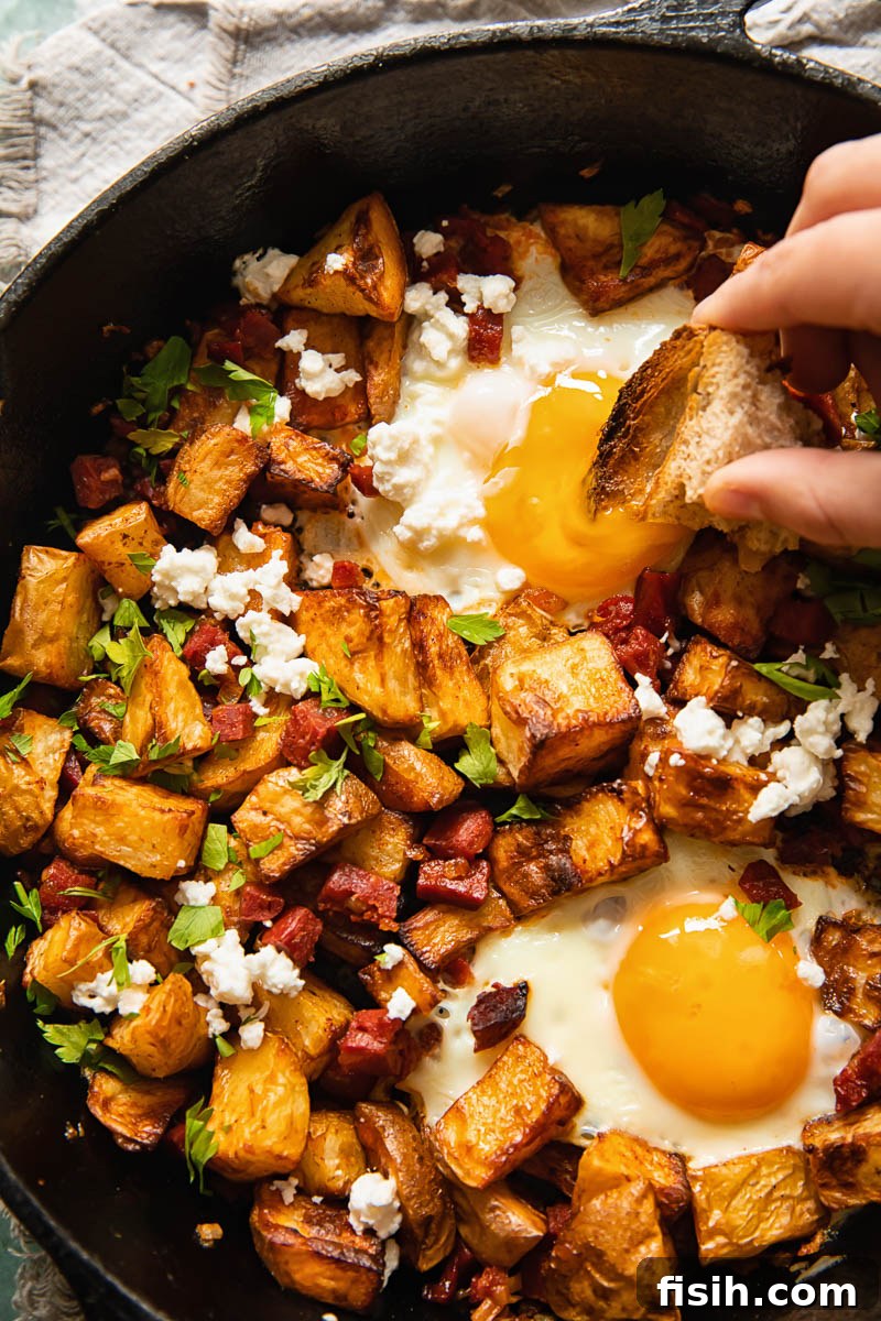 Savory Chorizo Hash with Tangy Feta 3 a hand dipping bread into an egg yolk and cubed potatoes in a pan