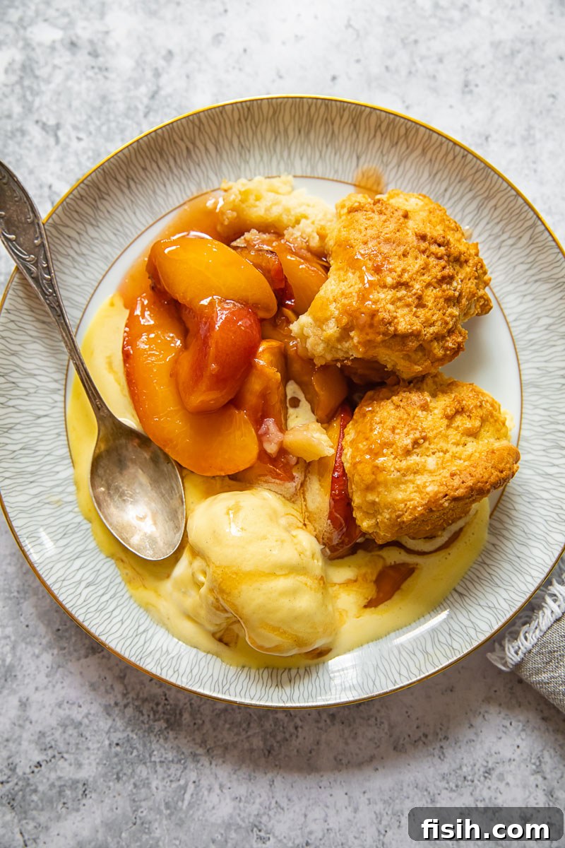 A serving of maple peach cobbler on a plate, topped with melted vanilla ice cream and a spoon.