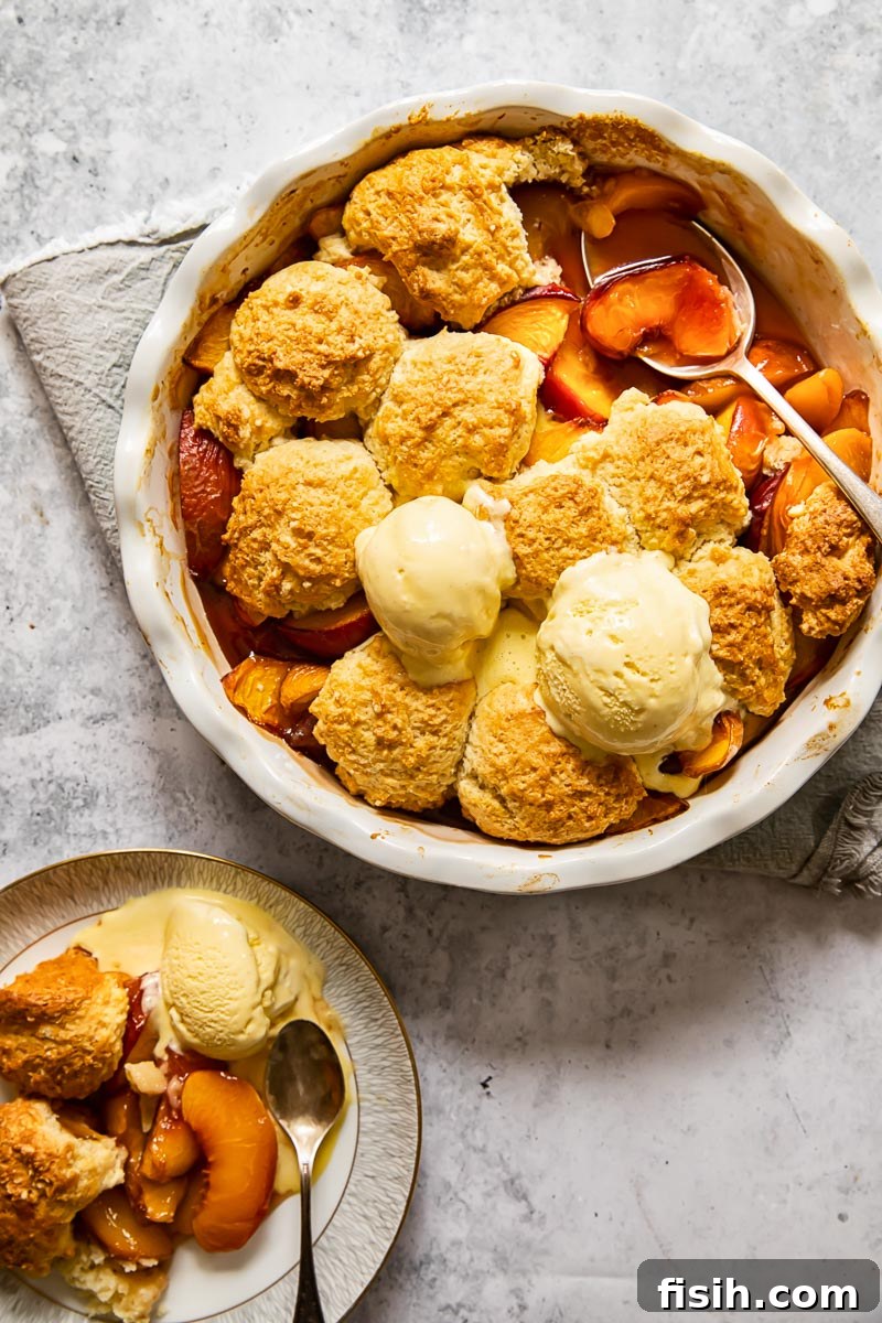 Top-down view of a maple peach cobbler garnished with two scoops of melting vanilla ice cream, ready to be enjoyed.