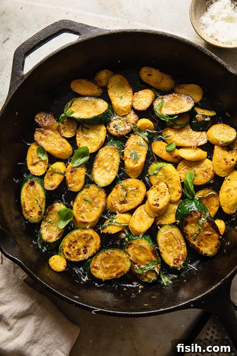 Golden Zucchini with Basil and Pecorino 4 Top-down view of vibrant yellow and green pan-fried zucchini rounds sizzling in a cast iron pan.