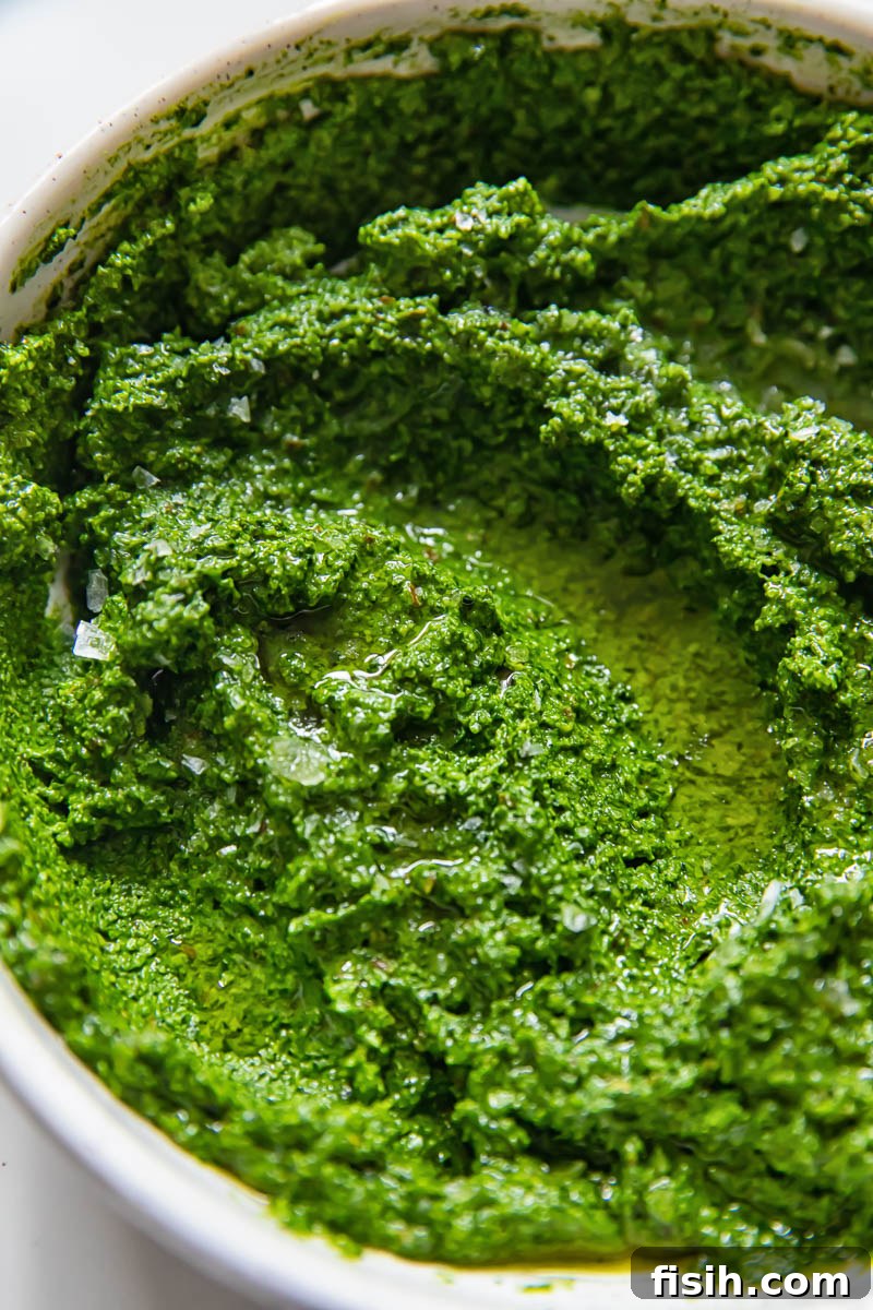 A vibrant green Tuscan kale pesto beautifully arranged in a rustic white bowl, ready to be enjoyed. The deep color hints at the rich, earthy flavors within.