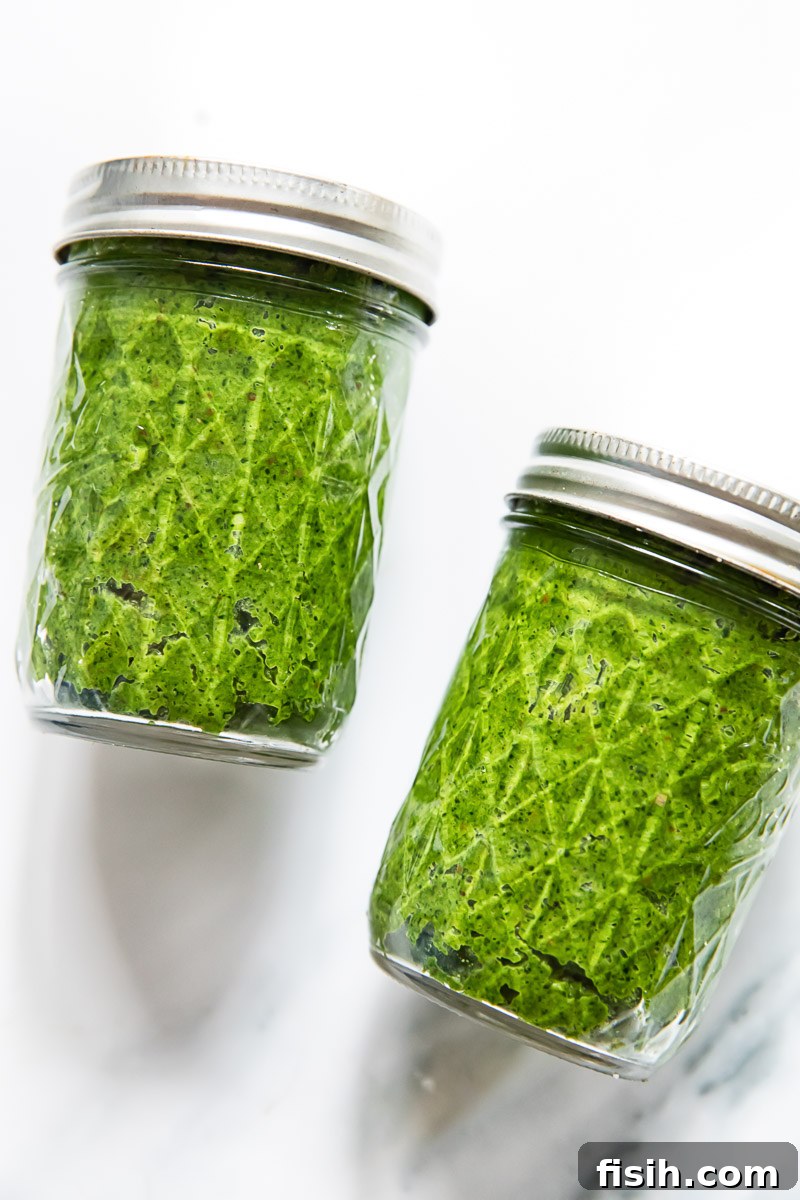 Two clear glass mason jars filled to the brim with vibrant green Tuscan kale pesto, showcasing its rich texture and color.
