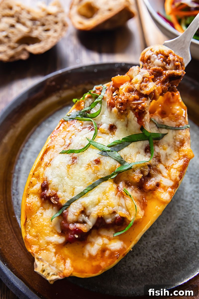 Top down view of a spaghetti squash half stuffed with rich bolognese sauce and topped with golden, melted mozzarella cheese, garnished with fresh herbs.
