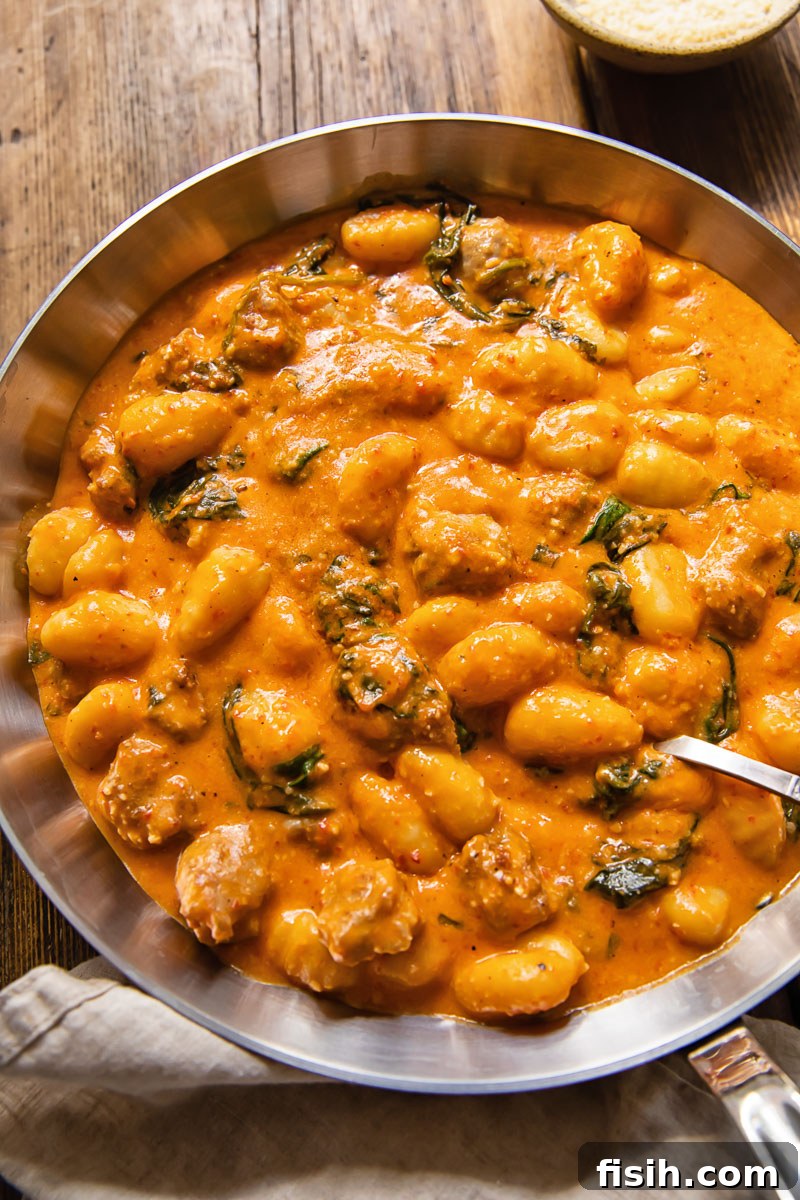 Pillowy Gnocchi & Sausage with Bold Romesco 4 Top-down view of a large skillet filled with cooked gnocchi and crumbled sausage, thoroughly coated in a rich Romesco sauce and garnished with fresh spinach.