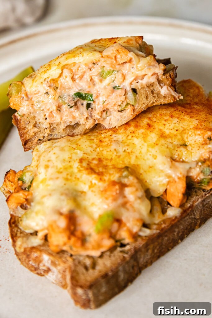 A delicious salmon sandwich, sliced in half, showcasing the cross-section with melted cheese, flaky salmon, and fresh ingredients.