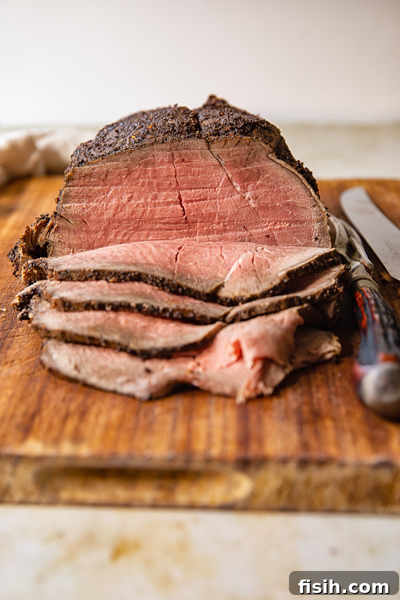 Slices of perfectly roasted top round beef, pink in the middle, alongside a whole roasted joint on a rustic cutting board, ready to be served at a holiday feast.