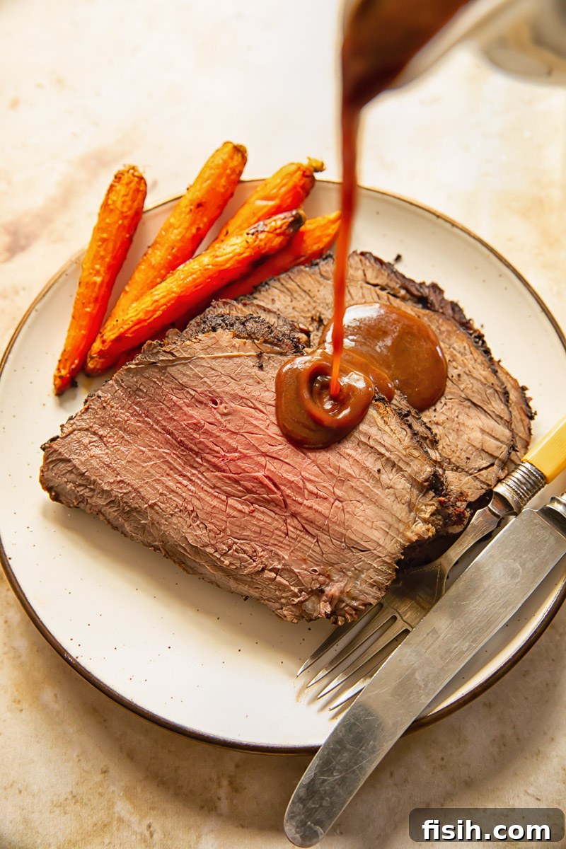 A stream of rich, brown gravy being poured over slices of tender roast beef on a white plate, ready to be enjoyed.