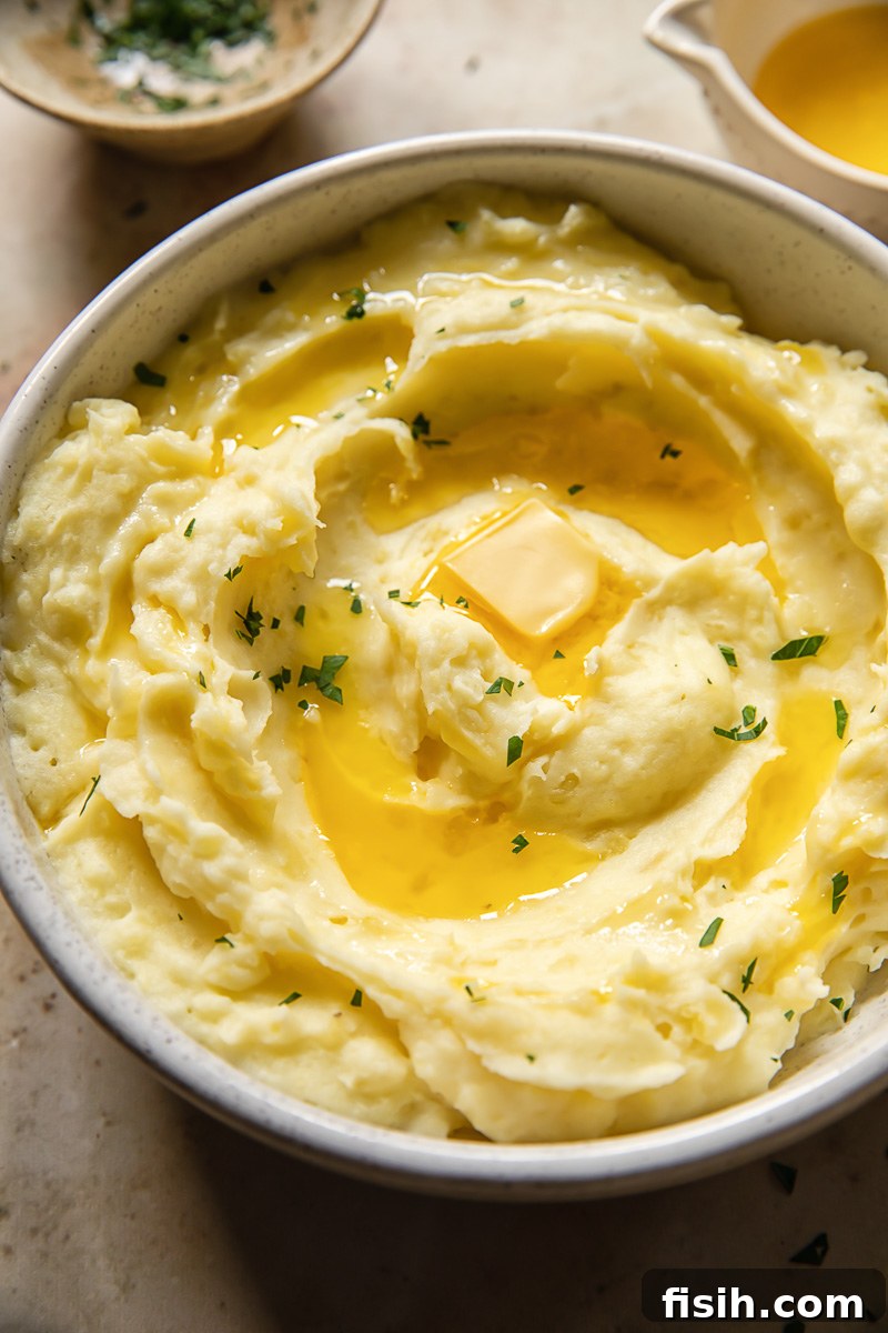 Velvety Instant Pot Mashed Potatoes 2 Top down view of perfectly fluffy mashed potatoes in a rustic ceramic bowl, garnished with fresh herbs and a swirl of melted butter.