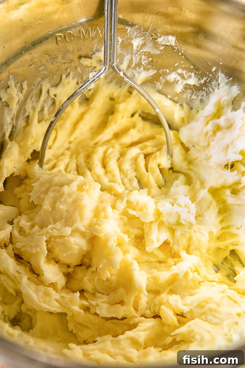 Velvety Instant Pot Mashed Potatoes 3 Close-up of fluffy potatoes being expertly mashed directly in the Instant Pot's inner pot, demonstrating hands-on preparation.