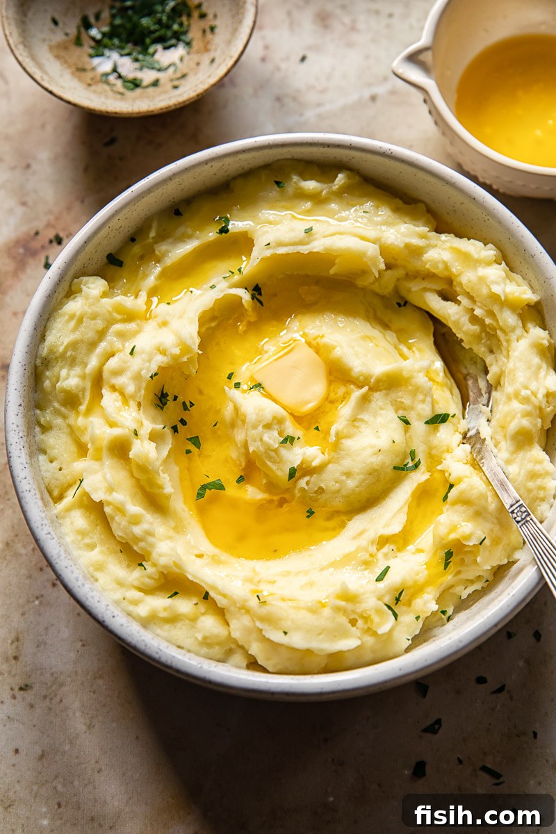 Velvety Instant Pot Mashed Potatoes 5 Close-up of a bowl of luxurious creamy mashed potatoes, elegantly drizzled with golden melted butter and sprinkled with vibrant fresh chopped parsley, ready to be served.