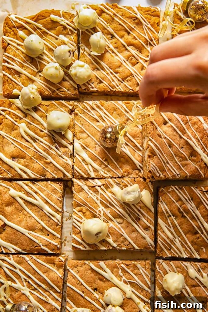 A hand carefully adding decorative white chocolate drizzle and whole hazelnuts to the cut blondie squares