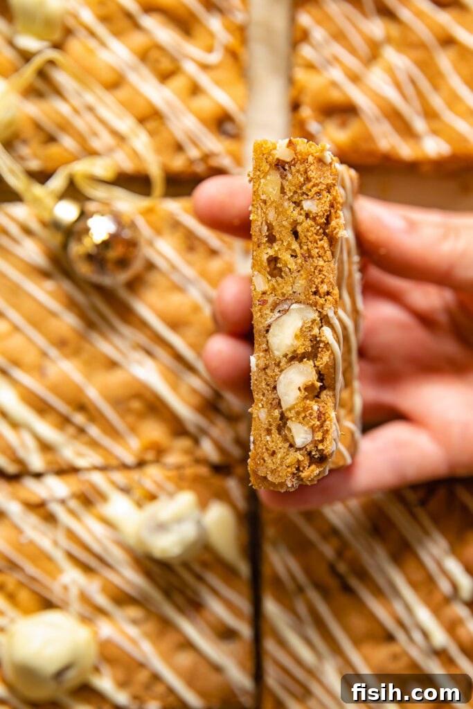 A hand holding a perfectly baked hazelnut blondie square, showing its chewy texture and hazelnut pieces