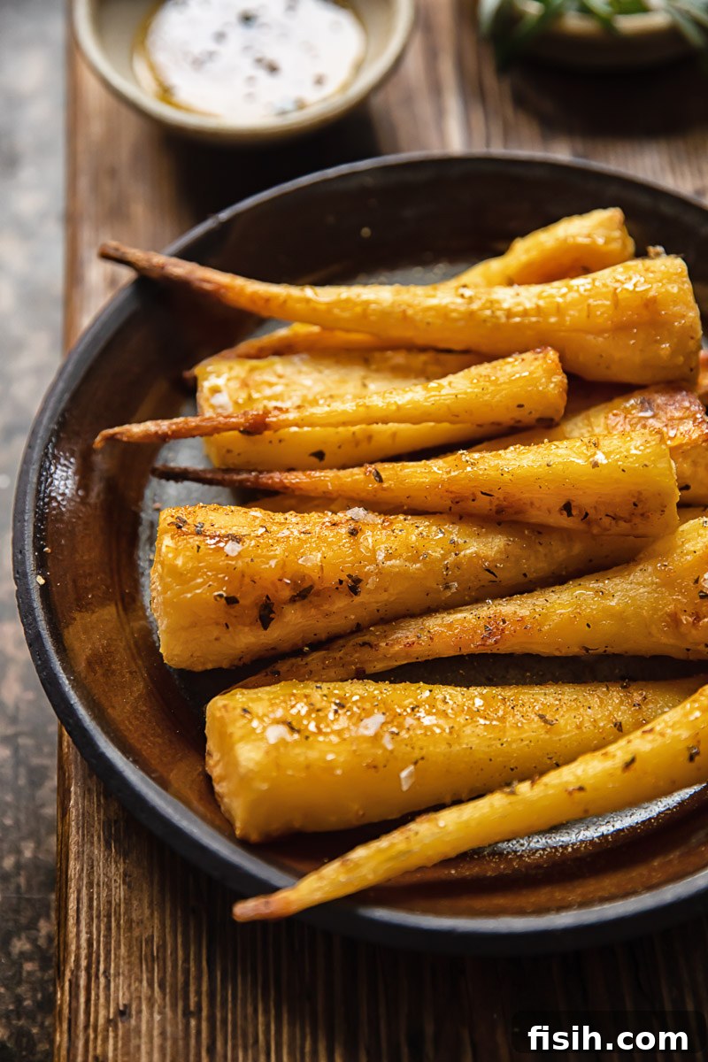 Caramelized Honey Garlic Parsnips 2 Golden brown roasted parsnips on a rustic brown plate, garnished with fresh rosemary. They appear crispy on the outside and tender within.