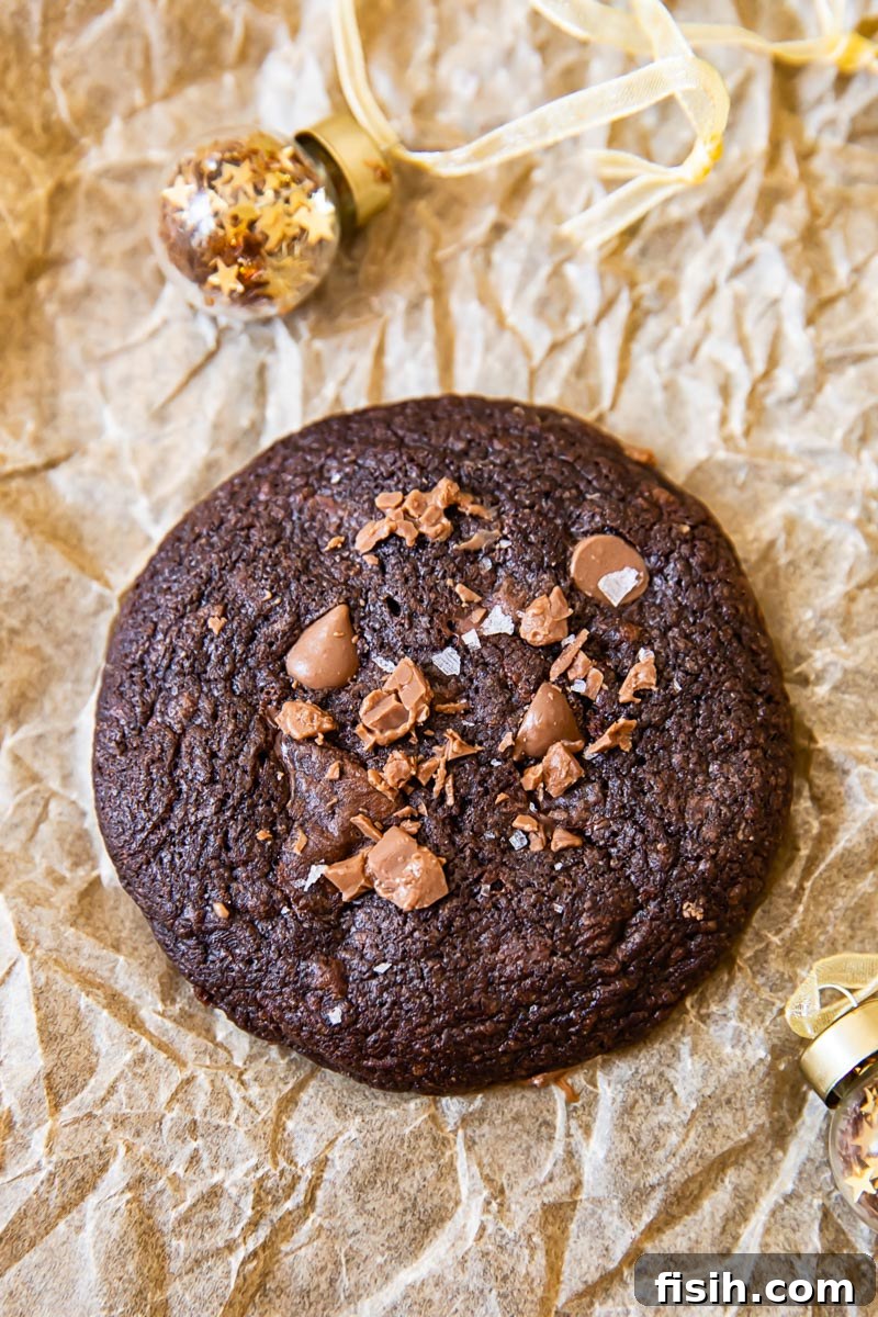 A single double chocolate mint cookie, perfectly round and dark, next to a miniature Christmas tree ornament, evoking holiday cheer.