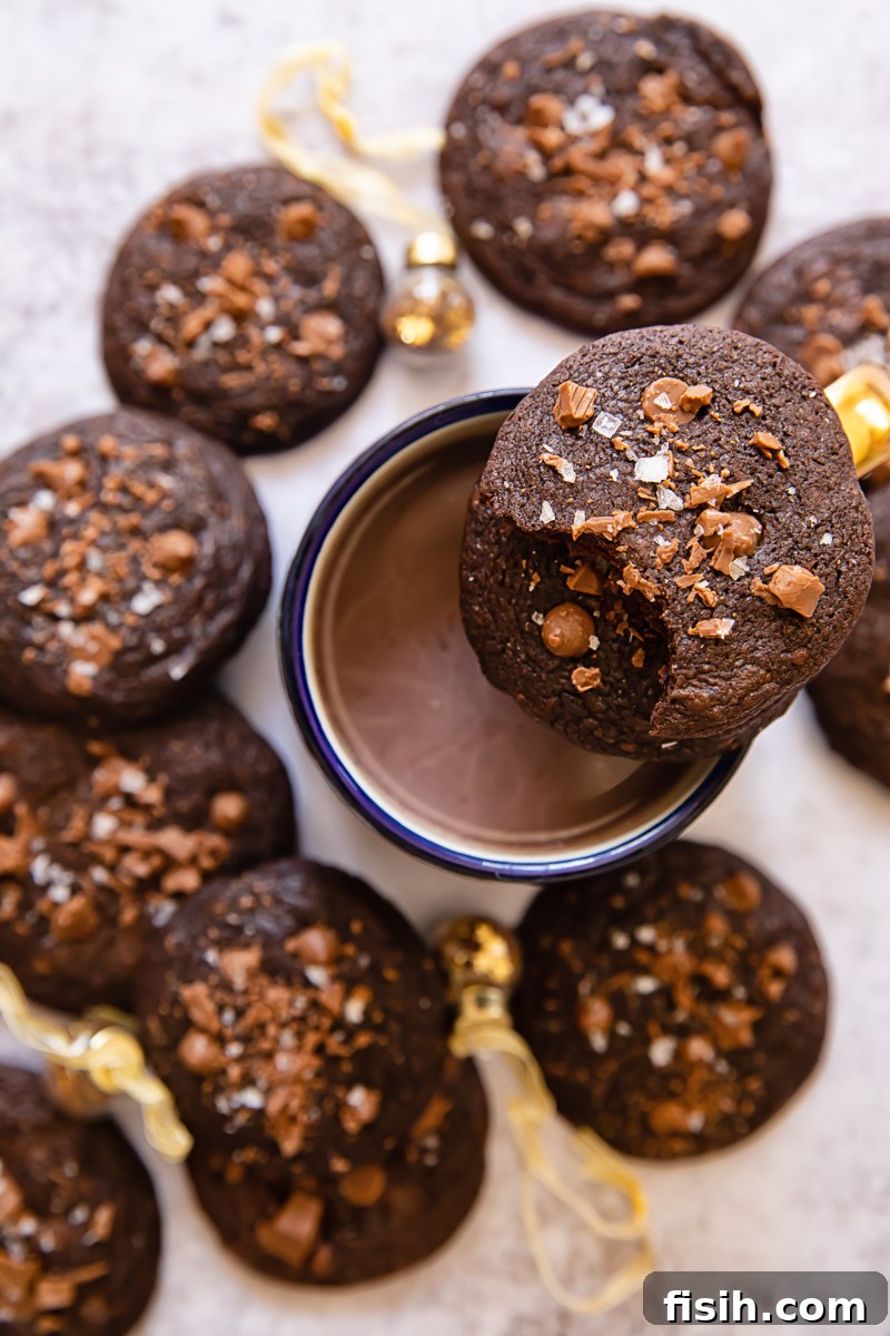 A festive arrangement of warm chocolate mint cookies around a mug of hot chocolate, with one cookie playfully balanced on the rim.