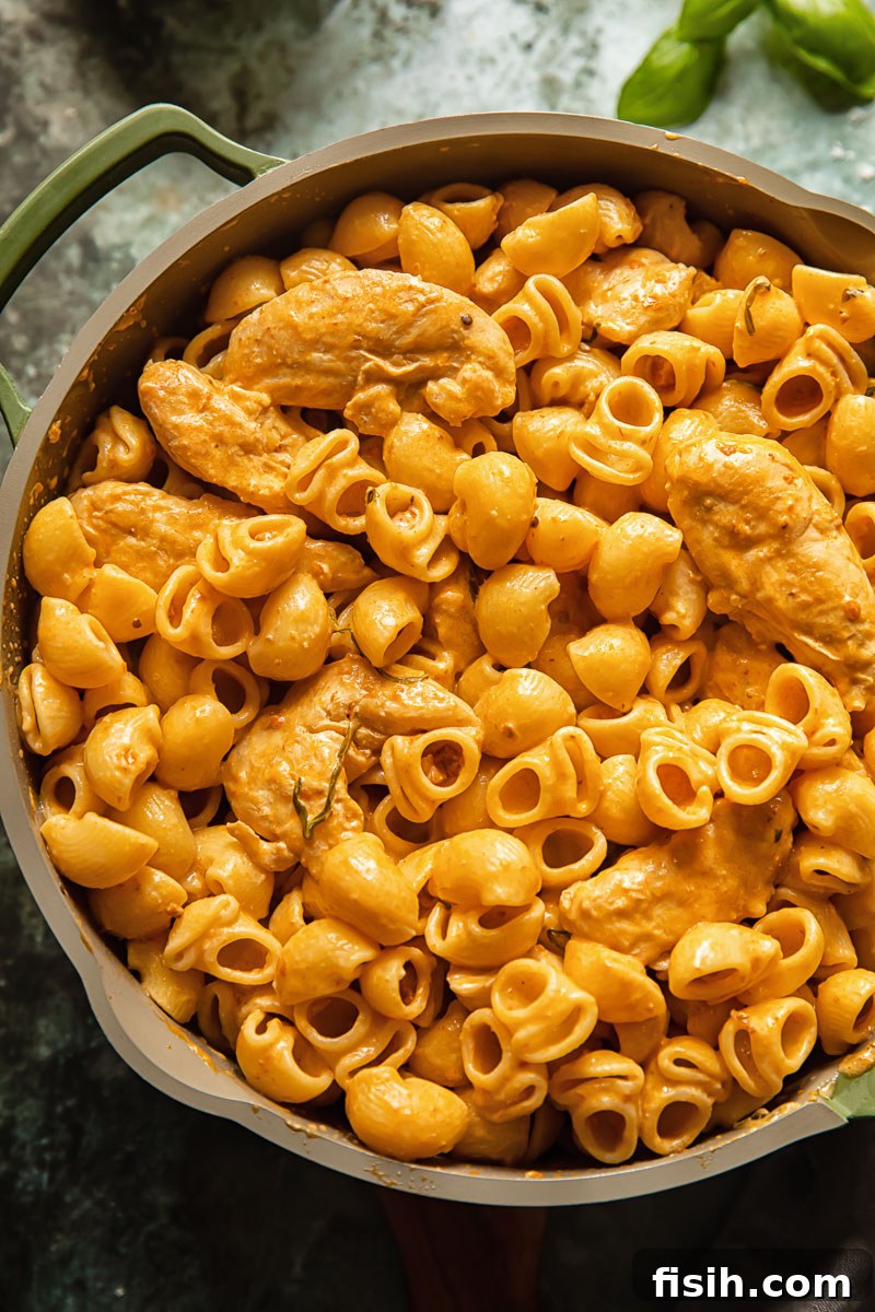 Top-down view of creamy tomato pasta with chicken and pancetta in a pan on a blue background