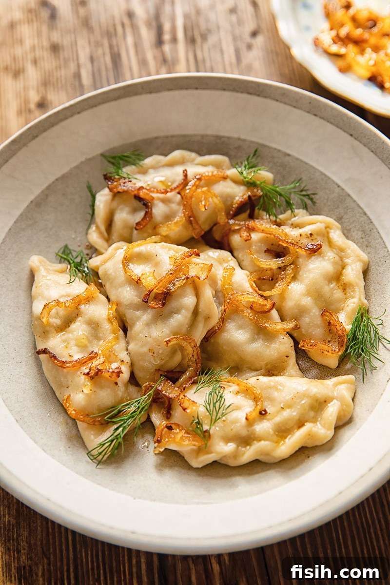 Tangy Sauerkraut and Earthy Mushroom Vareniki 2 Vareniki in a bowl, topped with fried onions and fresh dill, ready to be served.
