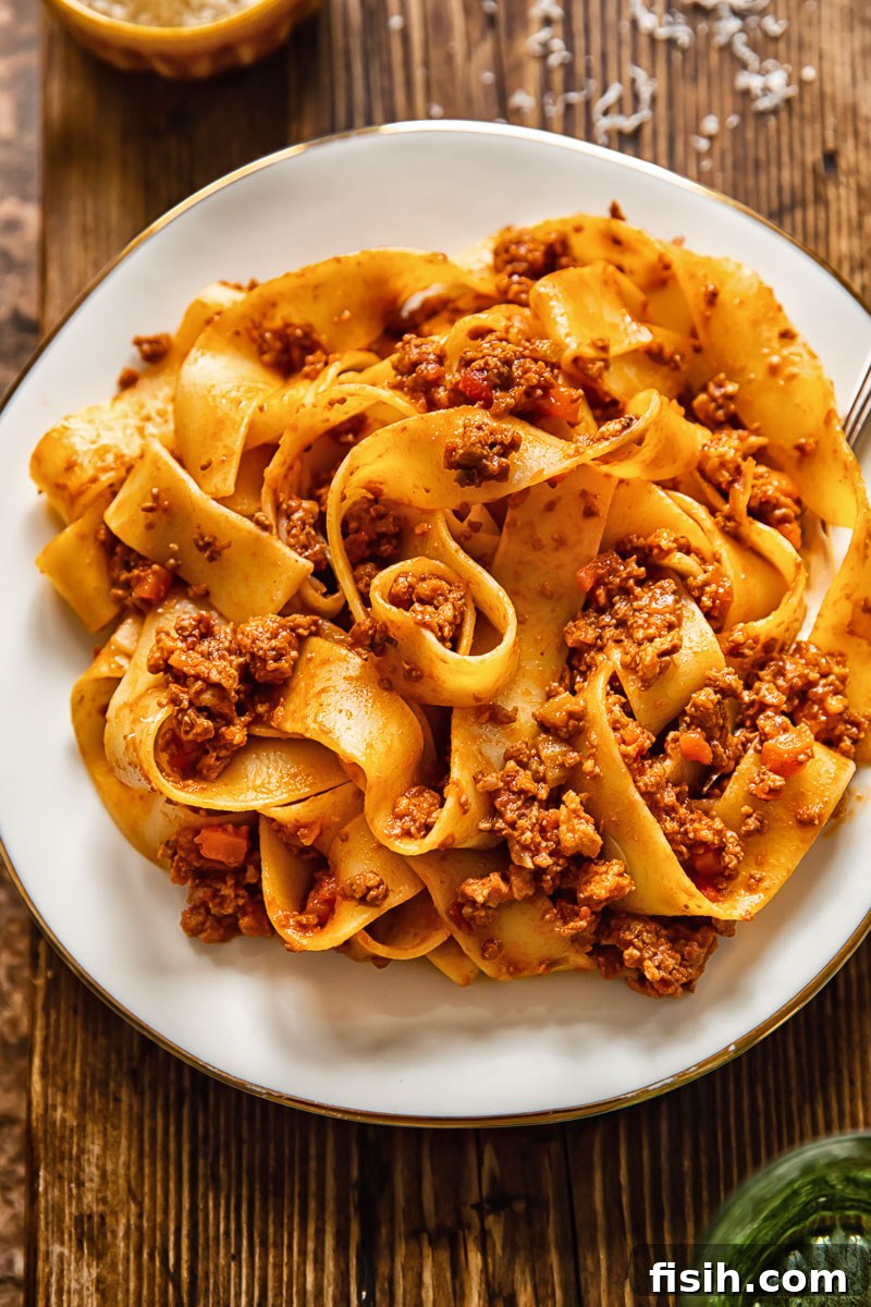 Top-down view of pappardelle pasta generously coated in a rich, meaty Tuscan ragu sauce on a white plate