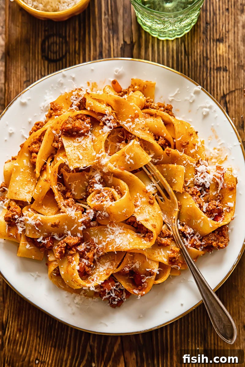 Top-down view of a white plate with pappardelle pasta generously topped with rich meat sauce
