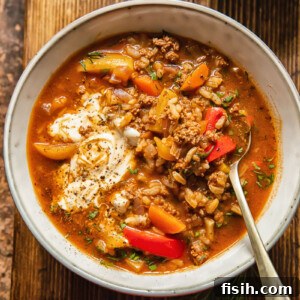 A vibrant bowl of deconstructed stuffed pepper soup, garnished with fresh herbs, with a spoon nestled in the bowl.